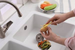 Person peeling vegetables onto a recently installed garbage disposal