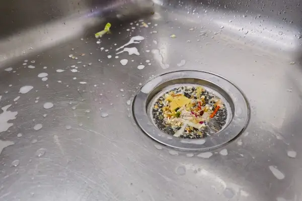 Close-up of a stainless steel kitchen sink with food scraps collected in a mesh drain strainer